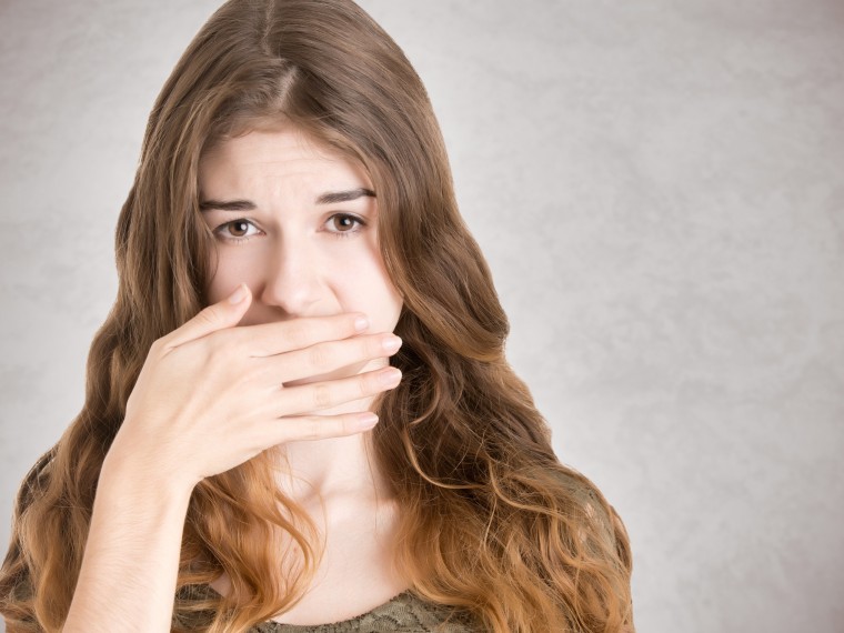 Frau bedeckt Mund mit Hand wegen Mundgeruch, schlechter Atem
